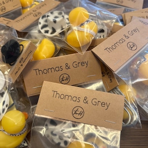 May include: A collection of small, yellow rubber duckies packaged in clear plastic bags with brown paper tags. The tags have the text "Thomas & Grey" and a logo with the letters "T&H".