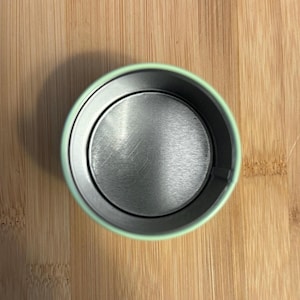 May include: The inside of a light green metal container with a silver bottom. The container is empty.
