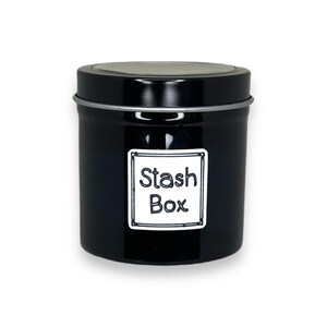 May include: A black metal tin with a silver rim and a white label that says "Stash Box".