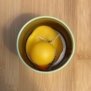 May include: A yellow rubber ducky with a white string attached to it is inside a green and gold tin can.