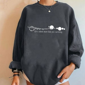 May include: Black sweatshirt with a white graphic of a key and planets with the text "Life is about more than just surviving".