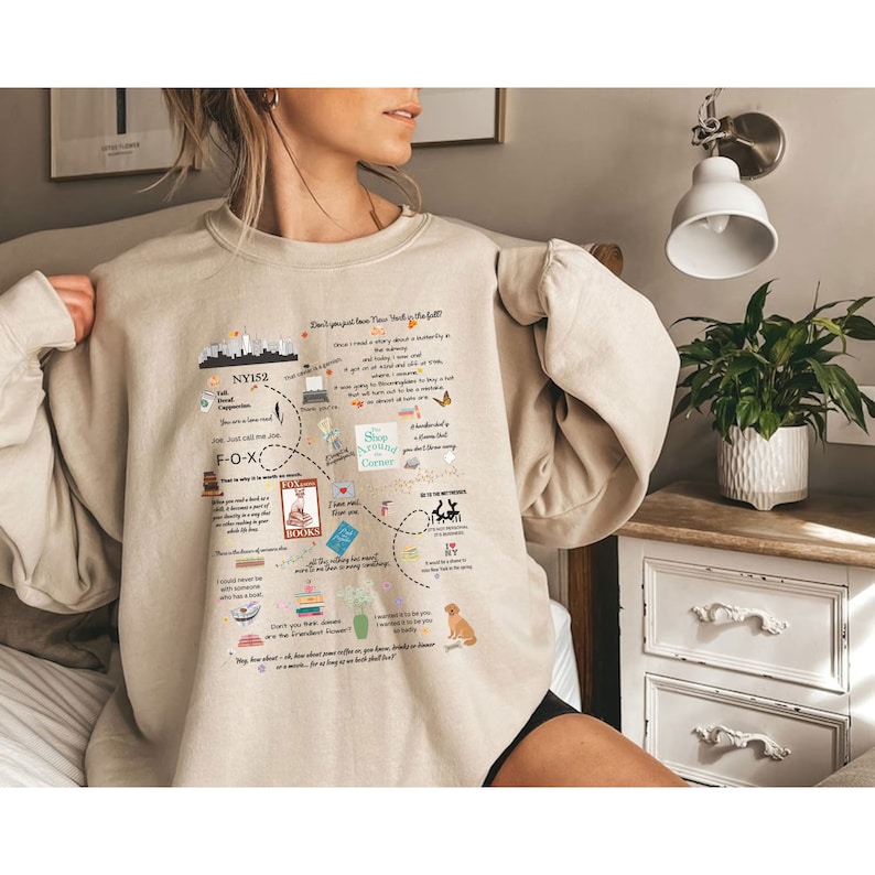Pode incluir: Camisola bege com um design gr&aacute;fico de um mapa da cidade de Nova Iorque com texto e ilustra&ccedil;&otilde;es. O texto inclui "Don't just love New York, live in the fall", "Shop Around the Corner", "I love NY" e "NY152".