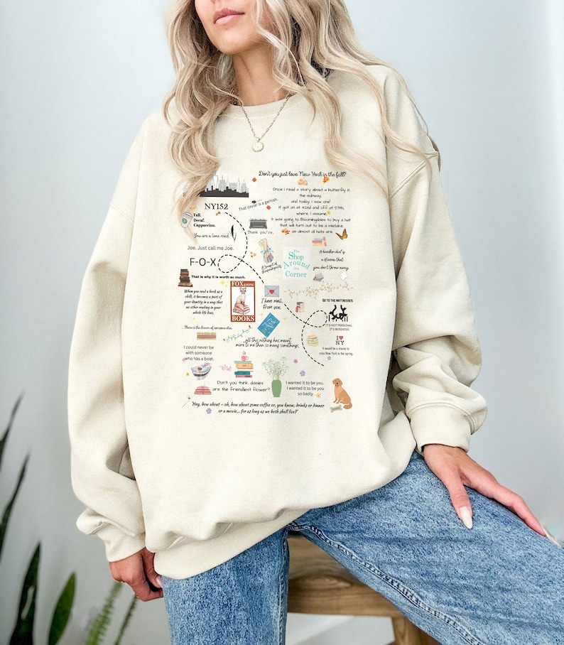 Pode incluir: Camisola bege com um design gr&aacute;fico que apresenta um mapa da cidade de Nova Iorque com v&aacute;rios marcos e cita&ccedil;&otilde;es. O design inclui o texto "Don't you just love New York in the fall?" e "Shop Around the Corner".