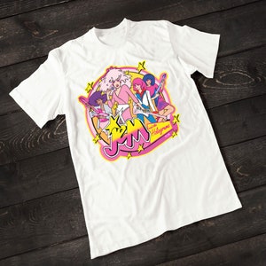 Może przedstawiać: Biała koszulka z r&oacute;żowym, ż&oacute;łtym i niebieskim nadrukiem przedstawiającym kresk&oacute;wkową grupę muzyczną Jem and the Holograms. Grafika przedstawia członk&oacute;w zespołu grających na instrumentach muzycznych oraz nazwę zespołu w stylizowanym foncie.