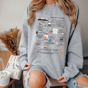 Pode incluir: Camisola de cor cinzenta com uma estampa gr&aacute;fica de um horizonte da cidade, livros e texto que diz "N&atilde;o apenas sonhe, seu trabalho &eacute; a mat&eacute;ria do outono".