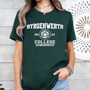 May include: A dark green t-shirt with white text that reads "Byrgenwerth MM XV College Fear the Old Blood". The text is surrounded by a graphic of an eye inside a triangle.