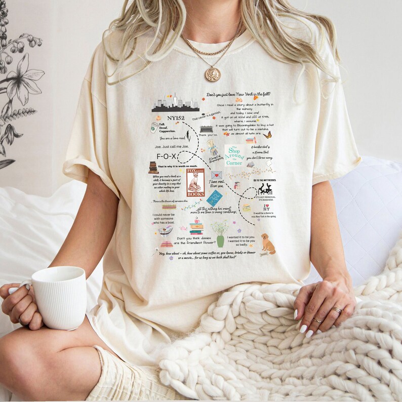 Pode incluir: Uma camiseta bege com um design gr&aacute;fico que apresenta um mapa da cidade de Nova Iorque com texto que diz "Don't you just love New York in the fall?" e "Shop Around Corner".