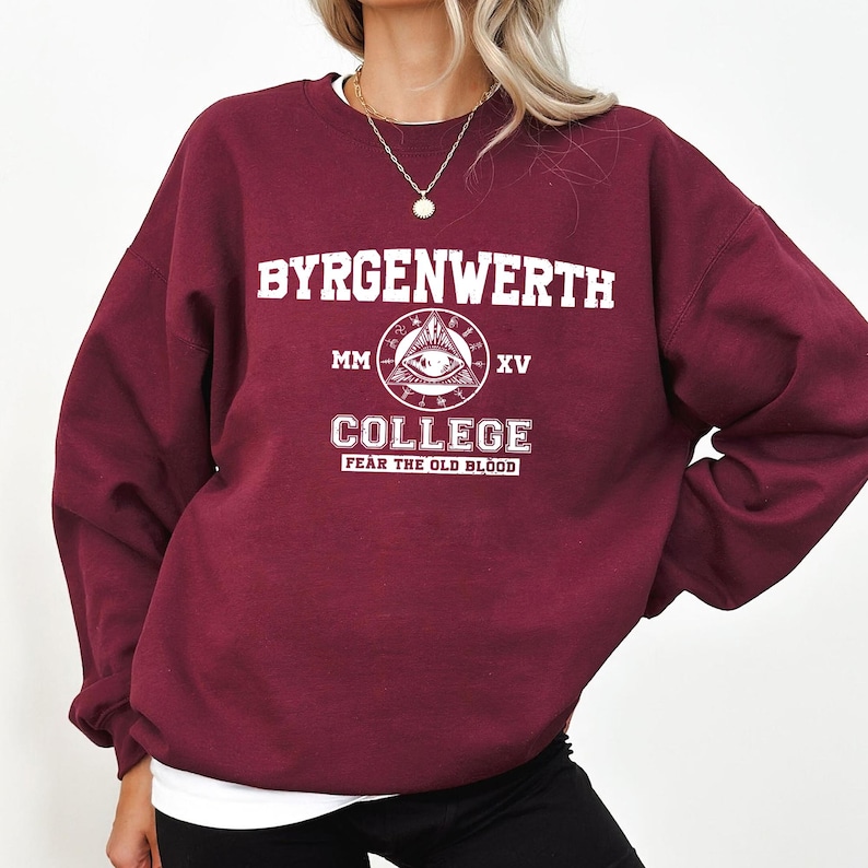 May include: Burgundy sweatshirt with a white graphic print that says "Byrgenwerth College MM XV Fear the Old Blood". The graphic features an eye inside a triangle.