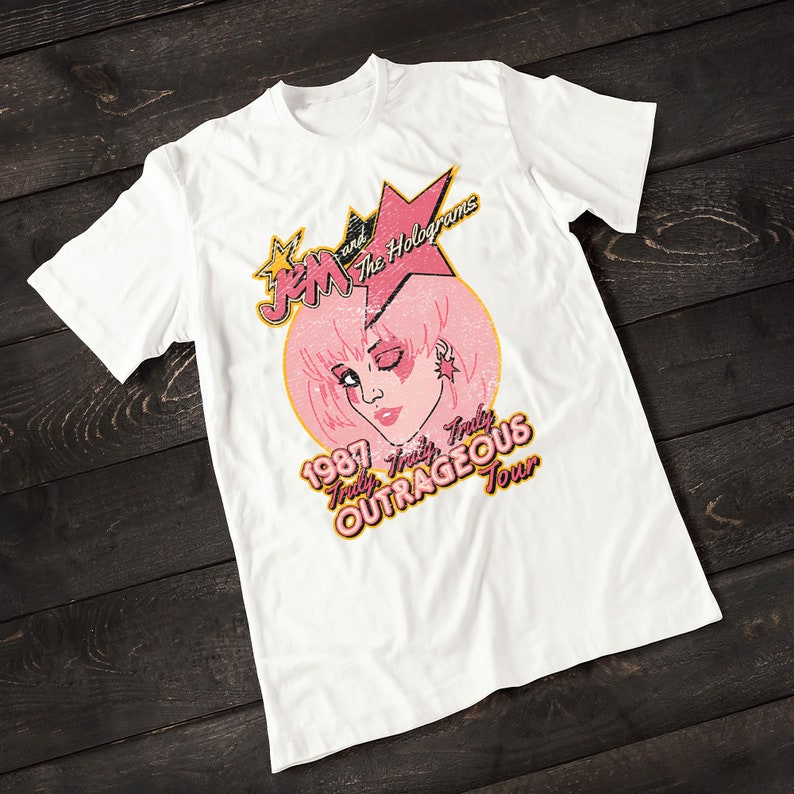 May include: White t-shirt with a vintage-style graphic of Jem and the Holograms. The graphic features a pink-haired Jem with a star and the text "1987 Truly Truly OUTRAGEOUS Tour".