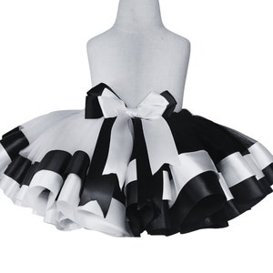 May include: A black and white tulle tutu skirt with alternating black and white satin ribbon trim. The skirt has a white satin bow at the back.