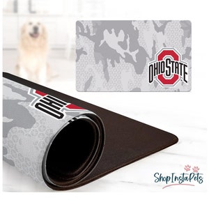 May include: A gray and white camouflage pattern mousepad with the Ohio State logo in red and white. The mousepad is rolled up, revealing a brown underside. The words "Shop Insta Pets" are in the bottom right corner.