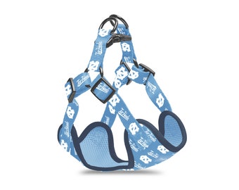 May include: Light blue dog harness featuring a repeating pattern of white logos and the text "Tar Heels." The harness has black plastic buckles and metal rings. The edges are trimmed with a darker blue fabric.