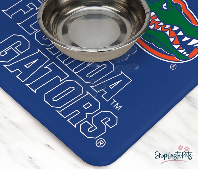 May include: Blue and white pet bowl mat with the University of Florida Gators logo and the words "Florida Gators" in white. The mat has a silver bowl on top of it.