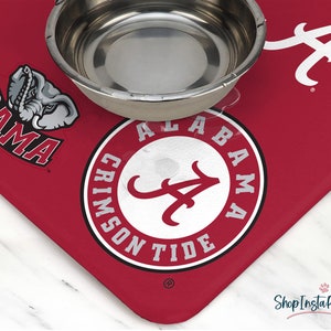May include: Red and white pet bowl mat with the Alabama Crimson Tide logo and a small elephant graphic. The mat has the words "Bama" and "Alabama Crimson Tide" printed on it.