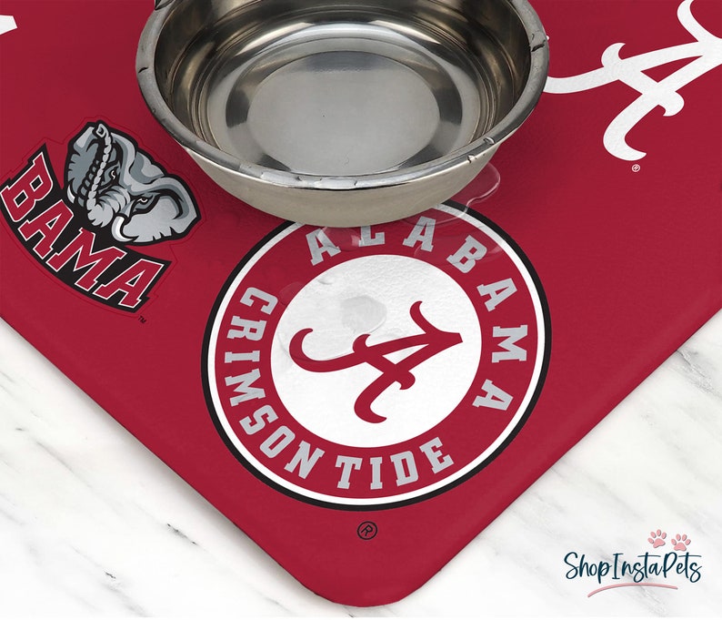 May include: Red and white pet bowl mat with the Alabama Crimson Tide logo and a small elephant graphic. The mat has the words "Bama" and "Alabama Crimson Tide" printed on it.