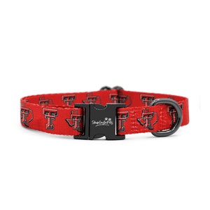 May include: Red dog collar with a black buckle and a repeating pattern of the Texas Tech University logo. The buckle has the text "Shop InstaPets" on it.
