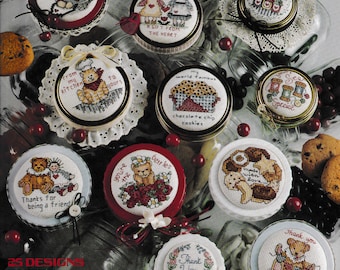 May include: A collection of 10 round jar lids with cross-stitch designs featuring bears, hearts, and other cute motifs. The lids are decorated with lace and ribbons. The text on the lids includes "Happincas is Homemade", "A Gift From The Heart", "From My Kitchen To Yours", "My World Famous Chocolate Chip Cookies", "Made With Love", "You're The Best", "Thanks For Being A Friend", "Thank You", and "Thank You With All My Heart".