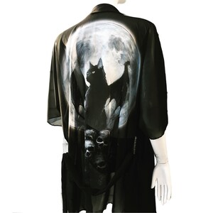 May include: Black chiffon kimono with a moon and a black cat with wings design. The cat is perched on a skull with other skulls below it.