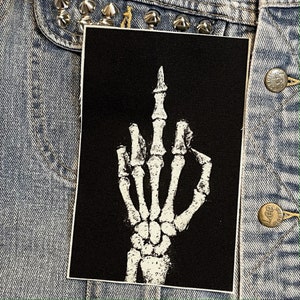 May include: Black and white embroidered patch of a skeleton hand giving the middle finger.