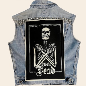 May include: A denim vest with silver studs and a black patch featuring a white skeleton with the text "Lewis Mayhem Born Dead".
