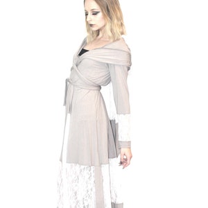 May include: A long, gray hooded wrap dress with a white lace trim. The dress has a tie belt and long sleeves. The model is wearing black heeled boots.
