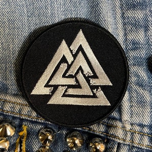 May include: A black and white embroidered patch featuring a triple triangle symbol, also known as the Valknut, on a black circular background.