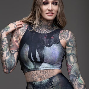 May include: A black crop top with a wolf graphic print. The wolf has red eyes and is set against a blue and purple galaxy-like background. The top has a racerback style and is made of a stretchy fabric.