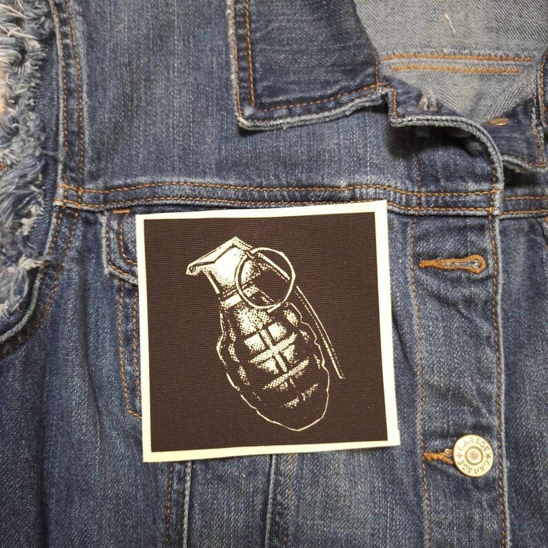 May include: A black and white embroidered patch of a grenade with a pull pin on a denim jacket.