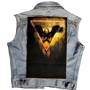 May include: A black and white patch with a woman with wings and a snake on her head. The woman is standing in a triangle with a halo above her head. The background is a dark yellow.