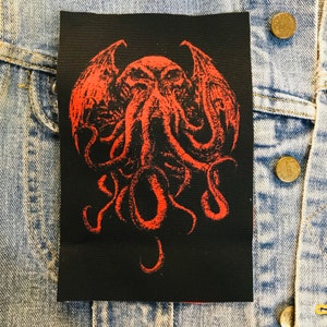 May include: Red and black embroidered patch featuring a winged, tentacled creature with a menacing expression. The creature is depicted in a detailed, stylized design.