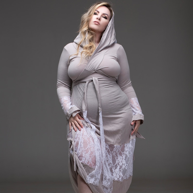 May include: A woman wearing a long, light gray hooded robe with a white lace trim. The robe is tied at the waist with a matching sash.