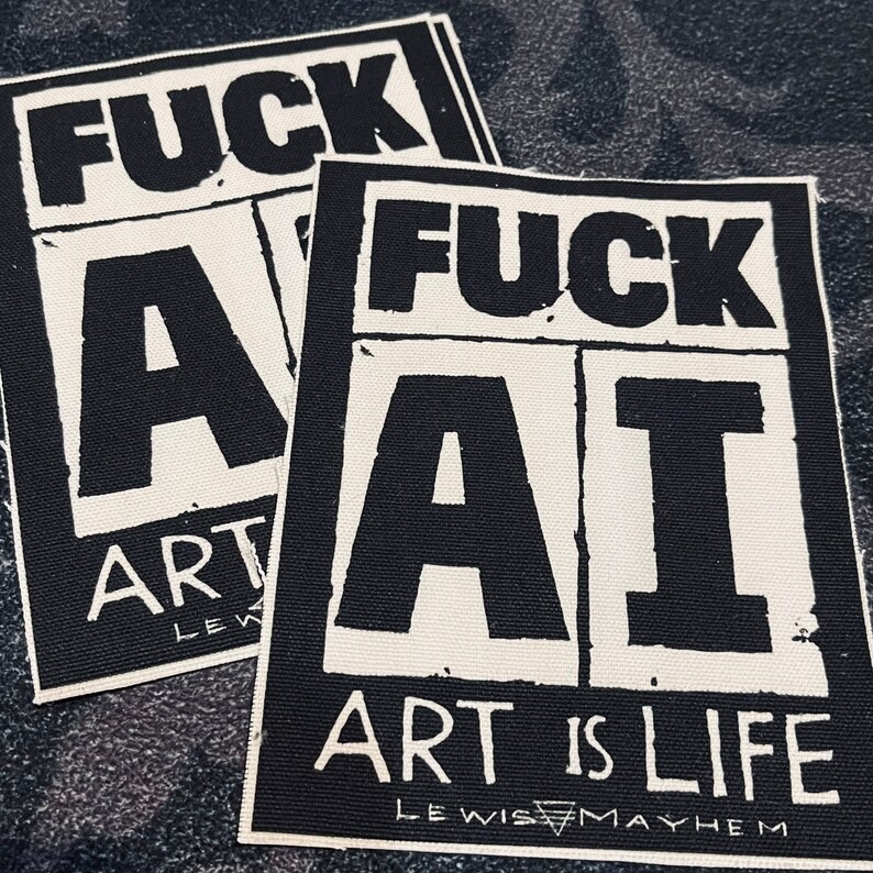May include: Two white fabric patches with black text. The top patch says "FUCK ART" and the bottom patch says "FUCK AI ART IS LIFE LEWIS MAYHEM".