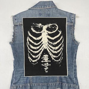 May include: A black fabric patch with a white ribcage design. The patch is sewn onto a denim vest.