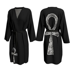 May include: Black robe with a white Ankh symbol on the back. The robe has a V-neck and long sleeves. The Ankh symbol is a stylized cross with a loop at the top.