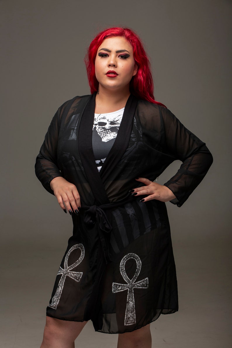 May include: Black sheer robe with an Ankh symbol design and a skull print on the inner lining. The robe has a tie closure at the waist.
