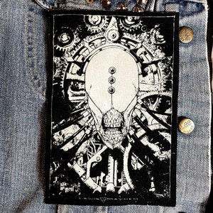 May include: Black and white patch featuring a detailed illustration of a skull with gears and machinery. The text "LEWIS MAYHEM" is at the bottom of the patch.