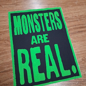 May include: A black rectangular patch with a green border and bold green text that reads "MONSTERS ARE REAL."