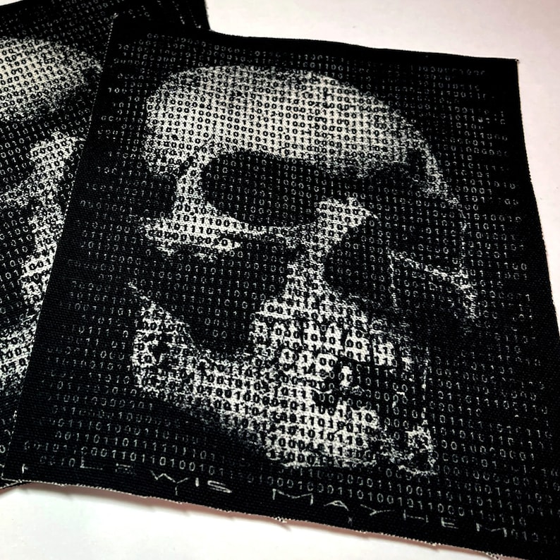 K&ouml;nnte beinhalten: Schwarz-wei&szlig; gestickter Patch mit einem Sch&auml;del-Design aus Bin&auml;rcode. Der Text "WISDOM" befindet sich am unteren Rand des Patches.