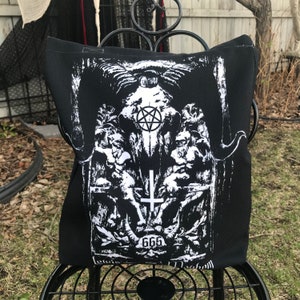 May include: Black tote bag with a white graphic print of a skull with a pentagram, a cross, and the number 666. The graphic is surrounded by a floral design.