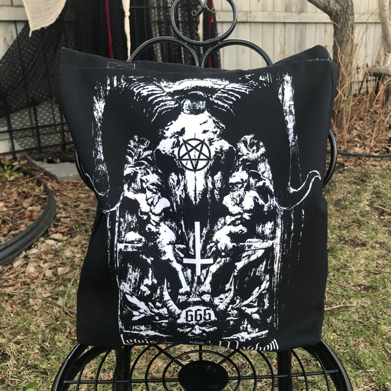 May include: Black tote bag with a white graphic print of a skull with a pentagram, a cross, and the number 666. The graphic is surrounded by a floral design.