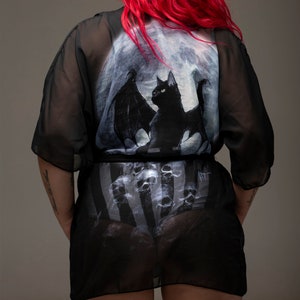 May include: Black sheer robe with a moon and black cat with wings print. The robe has a striped pattern underneath.