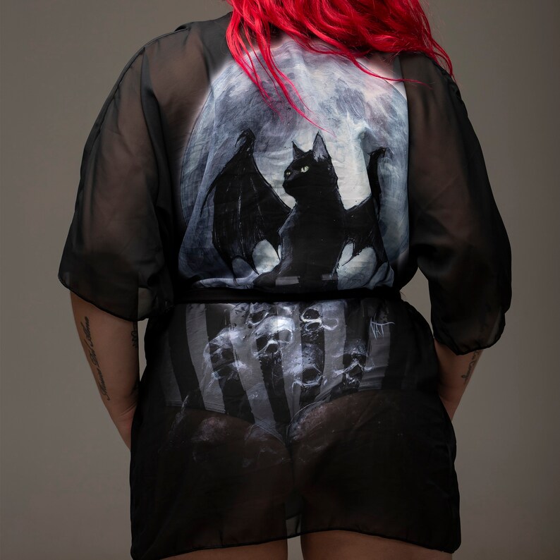 May include: Black sheer robe with a moon and black cat with wings print. The robe has a striped pattern underneath.