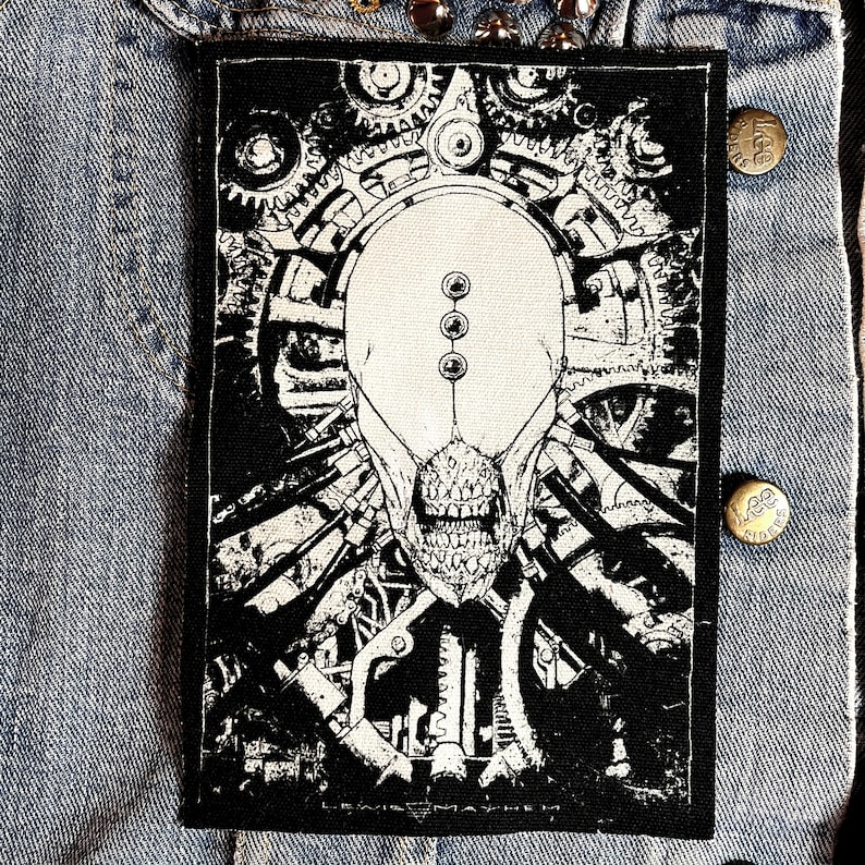 May include: Black and white patch featuring a detailed illustration of a skull with gears and machinery. The text "LEWIS MAYHEM" is at the bottom of the patch.
