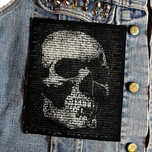 K&ouml;nnte beinhalten: Ein schwarz-wei&szlig;es Totenkopf-Patch mit einem bin&auml;ren Code-Muster. Das Patch hat den Text "WE ARE MAYHEM" unten.