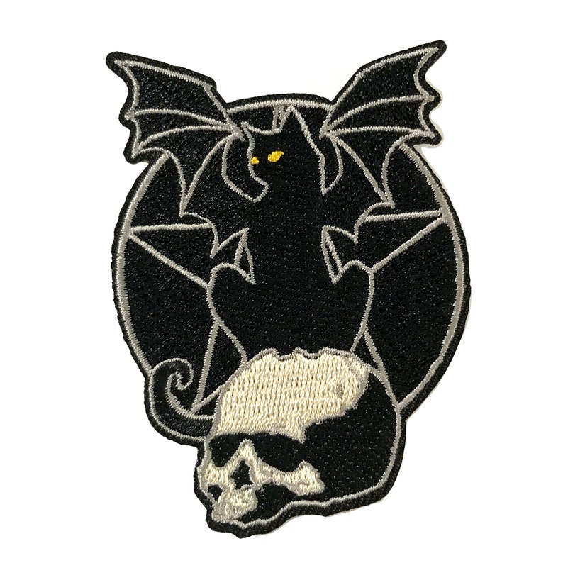 Pode incluir: Patch bordado preto e branco de um gato preto com asas, sentado em um cr&acirc;nio com um pentagrama atr&aacute;s.