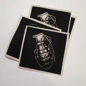 May include: Three black fabric patches with a white image of a hand grenade on each. The grenade is a stylised illustration with a pin and a handle.