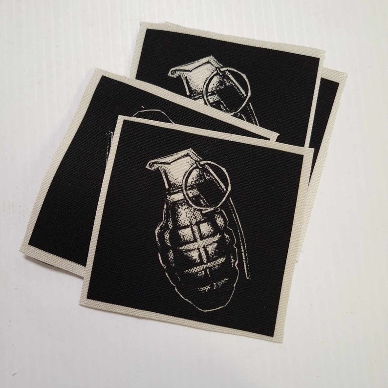 May include: Three black fabric patches with a white image of a hand grenade on each. The grenade is a stylised illustration with a pin and a handle.