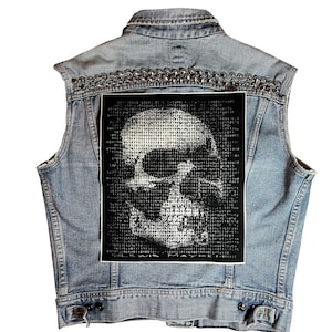 May include: A blue denim vest with a skull graphic patch on the back. The patch is black with a white skull made of binary code. The vest has silver studs around the collar and down the back.