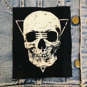 May include: A black and white skull patch with a triangle design and three horizontal lines across the eyes. The skull is in a distressed style.