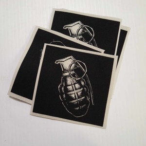 May include: Three black fabric patches with a white image of a hand grenade on each. The grenade is a stylised illustration with a pin and a handle.